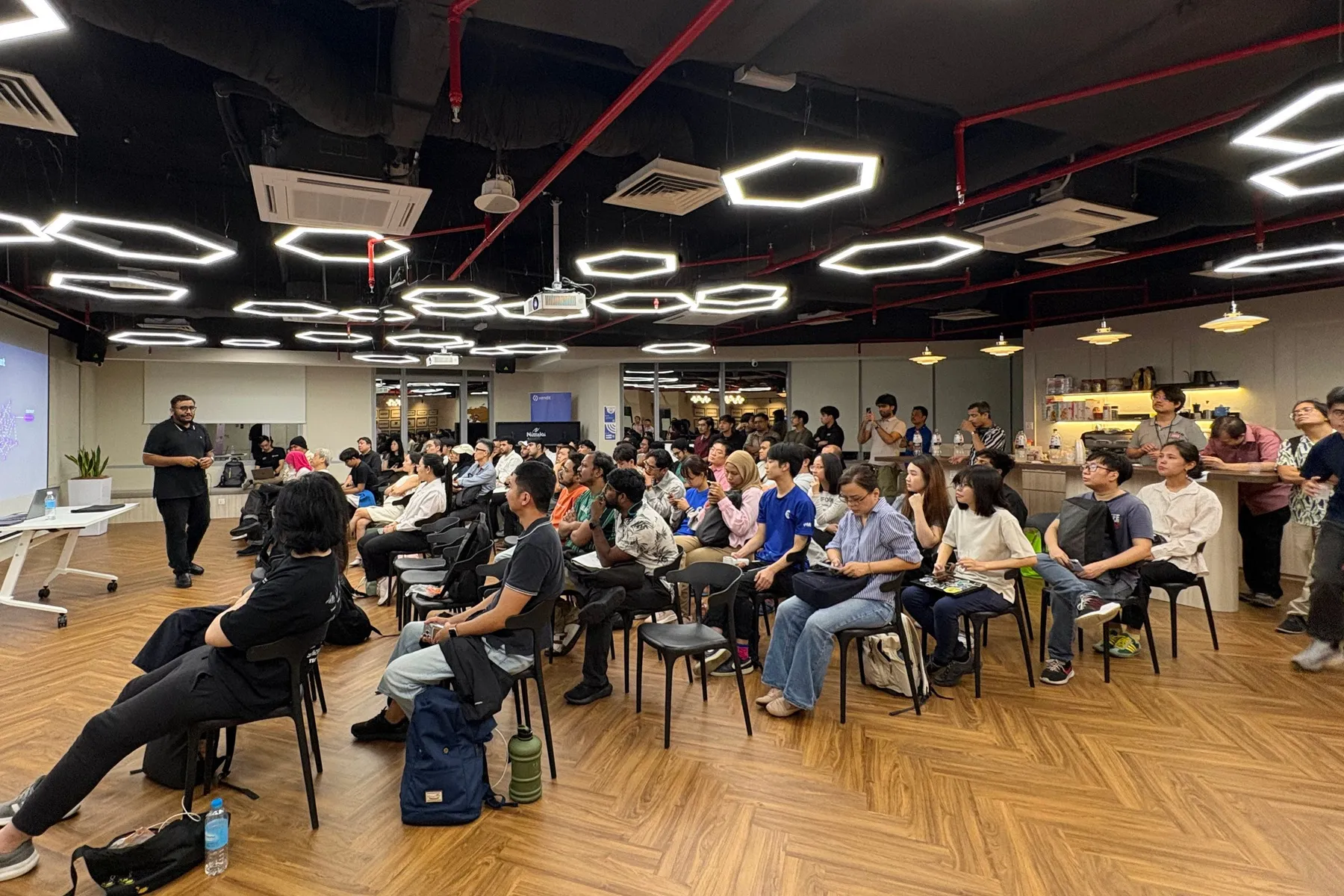 A speaker presents on spec-driven development to a full room under hexagon-shaped ceiling lights