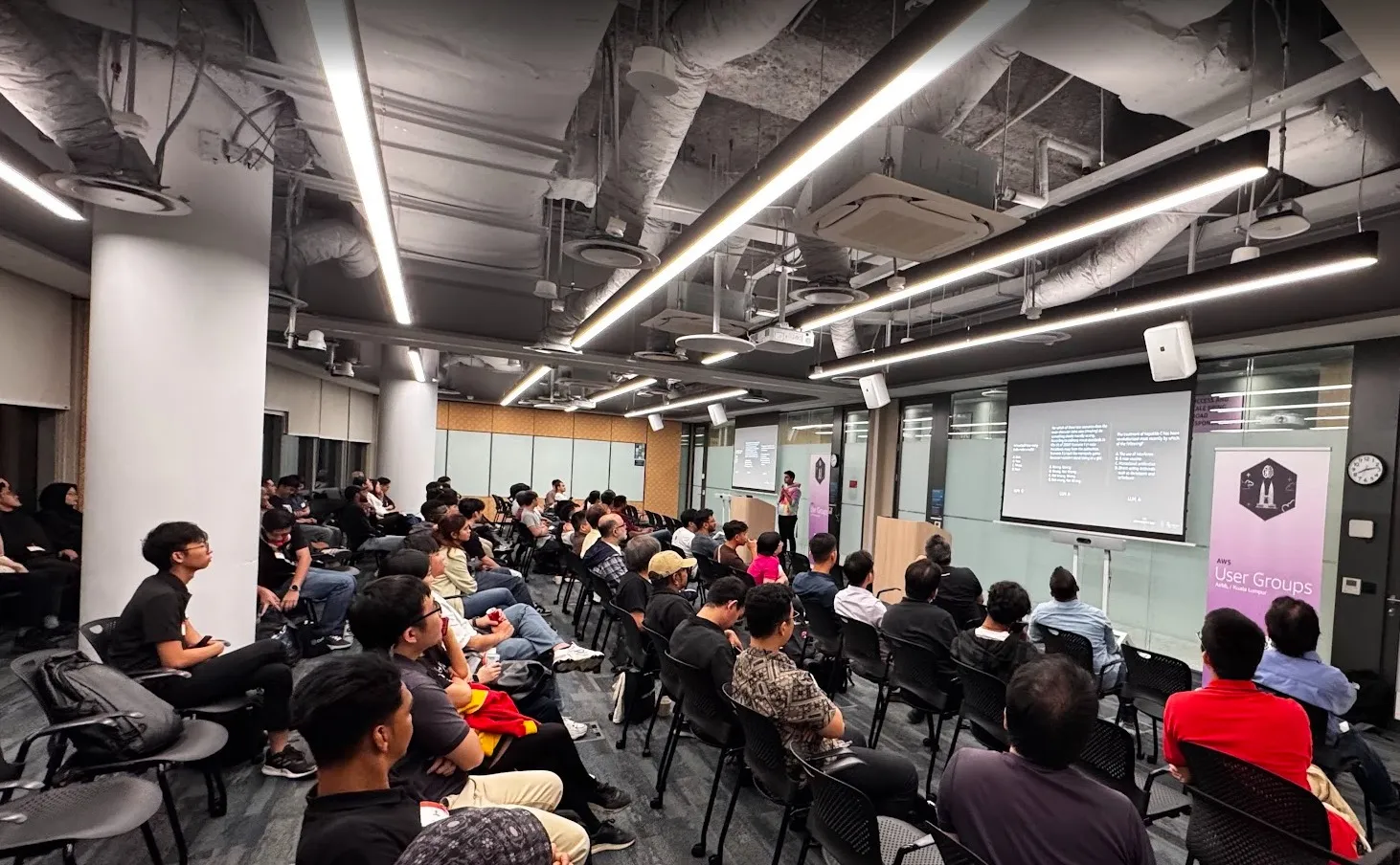 A full room of attendees watching a talk, with the AWS User Groups AI/ML Kuala Lumpur banner beside the screen